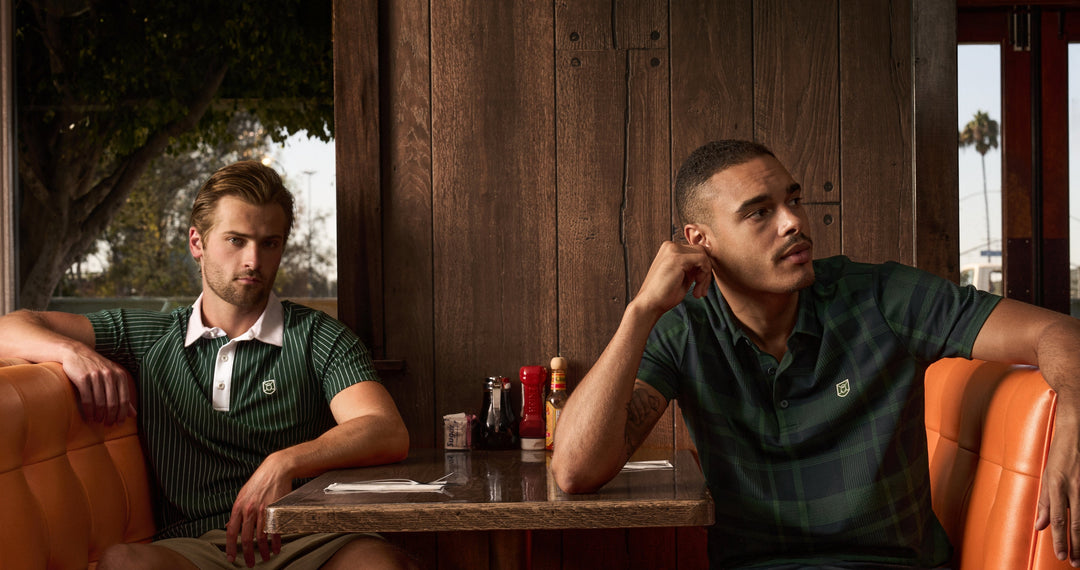 Lifestyle image of two male models sitting across from each other in a vintage diner, wearing Ghost Golf polos and posing with a relaxed, confident look.