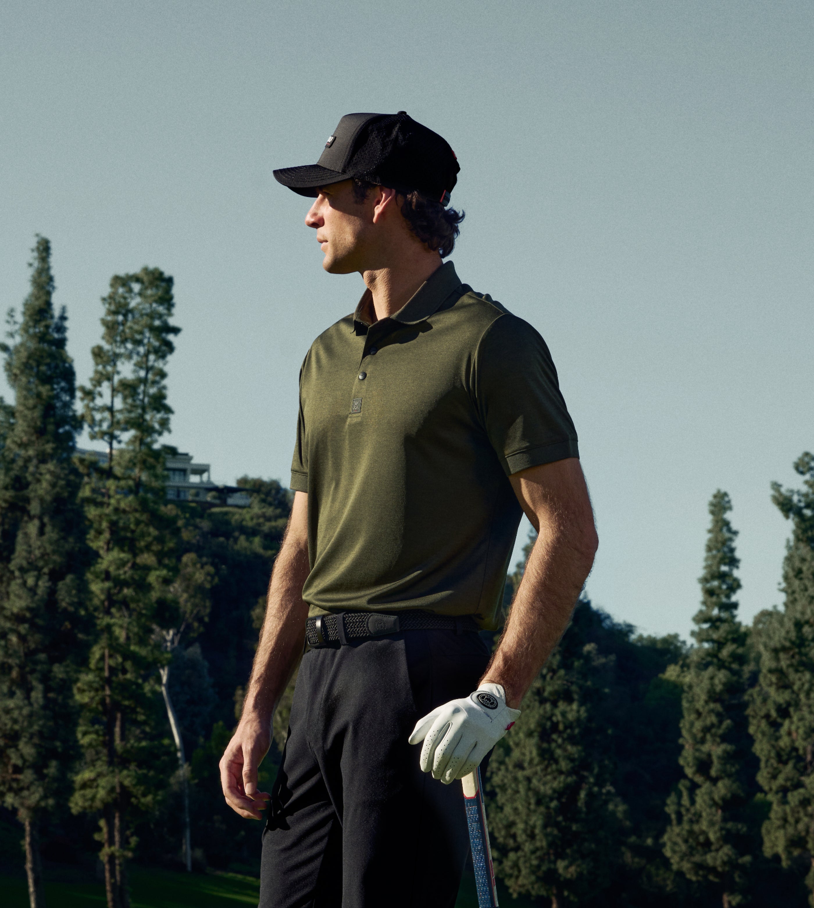 Man in golf attire standing on a golf course with trees in the background