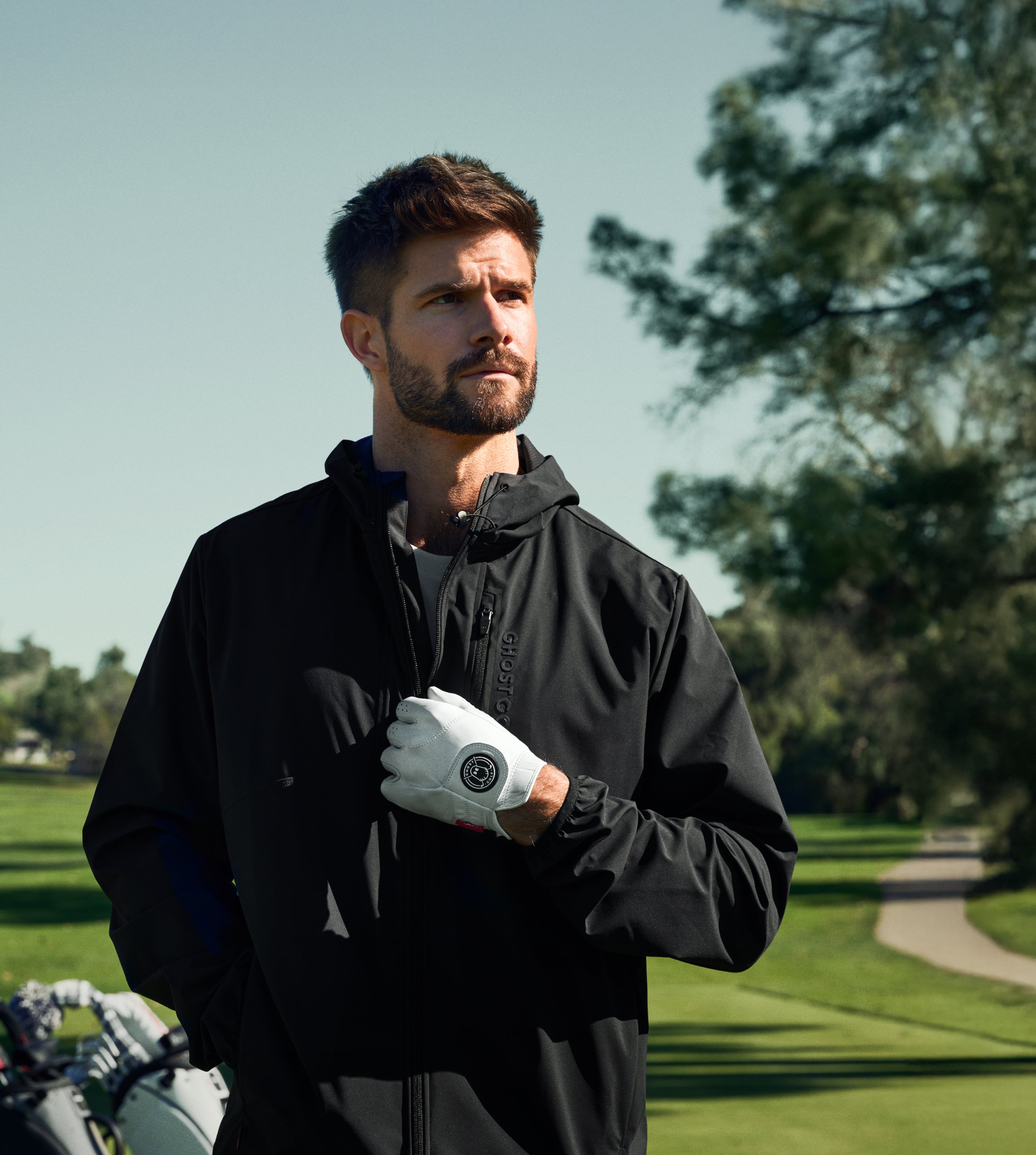 Man in black jacket wearing a white golf glove on a golf course