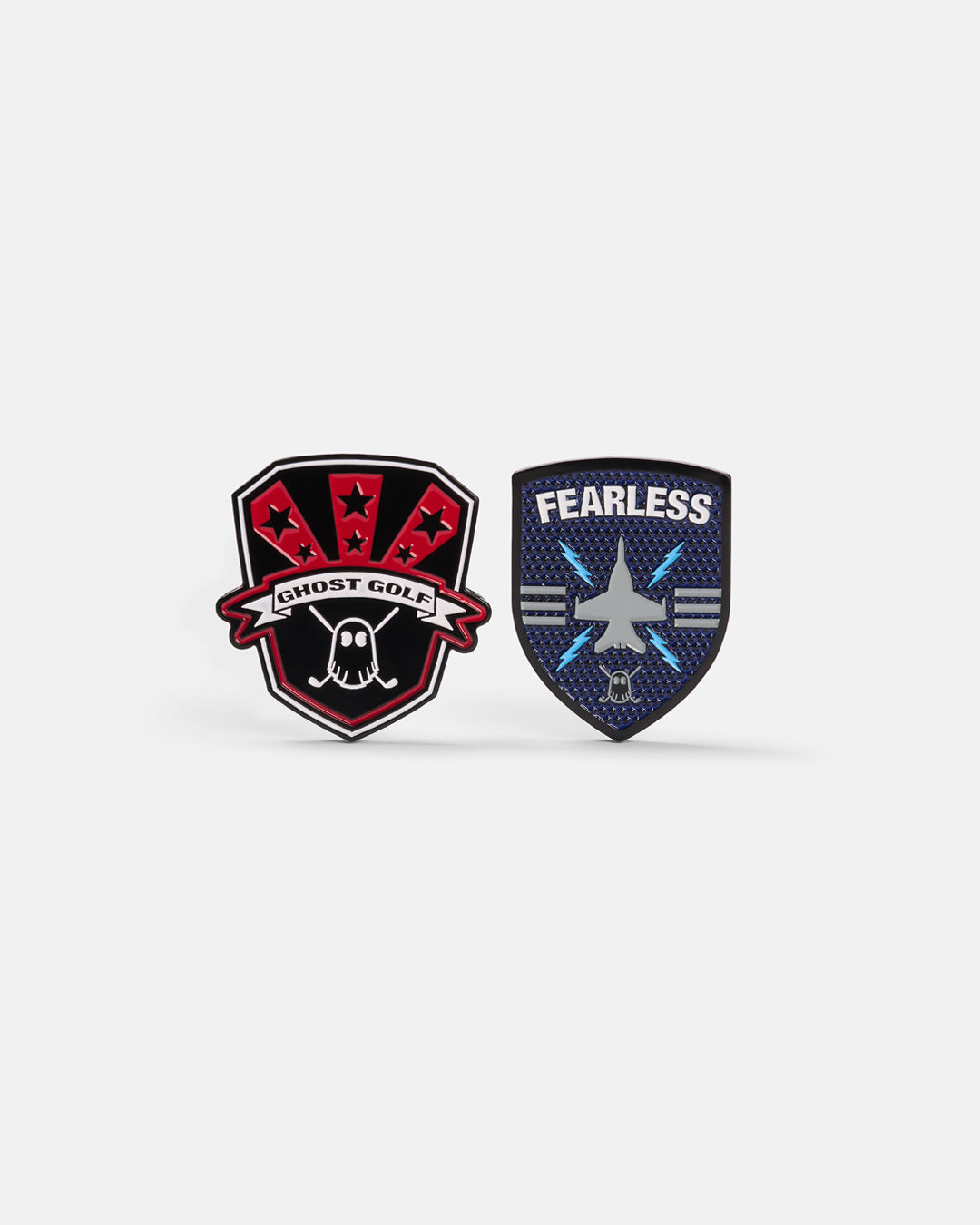 Product photo of two ball markers, one in a shield design featuring the word “Fearless,” a jet icon, and the Ghost Golf logo, alongside a black shield-shaped marker with red accents displaying the Ghost Golf name and logo.