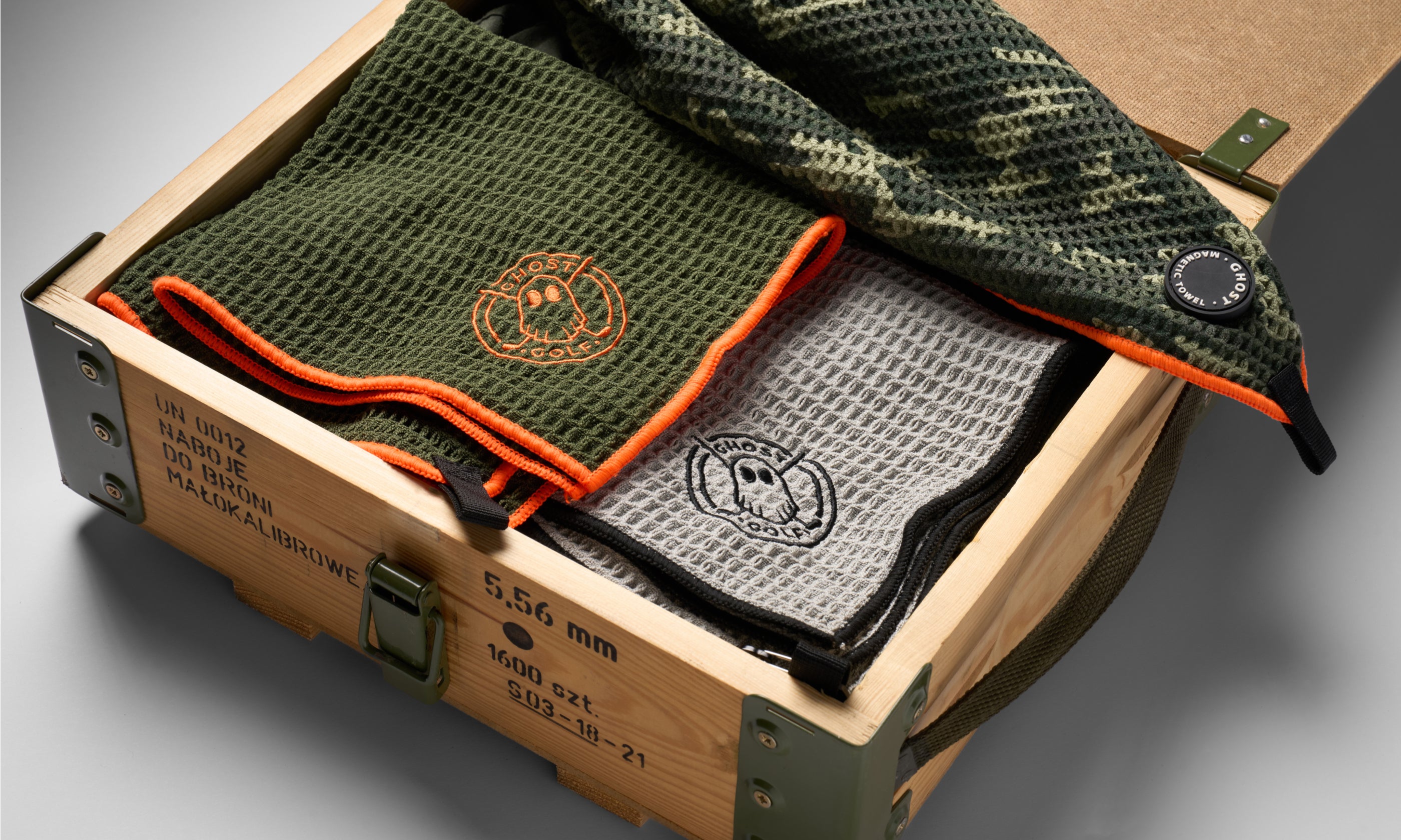 Studio product photo of Ghost Golf magnetic towels neatly folded inside a small wooden crate, with the Ghost Golf logo visible.
