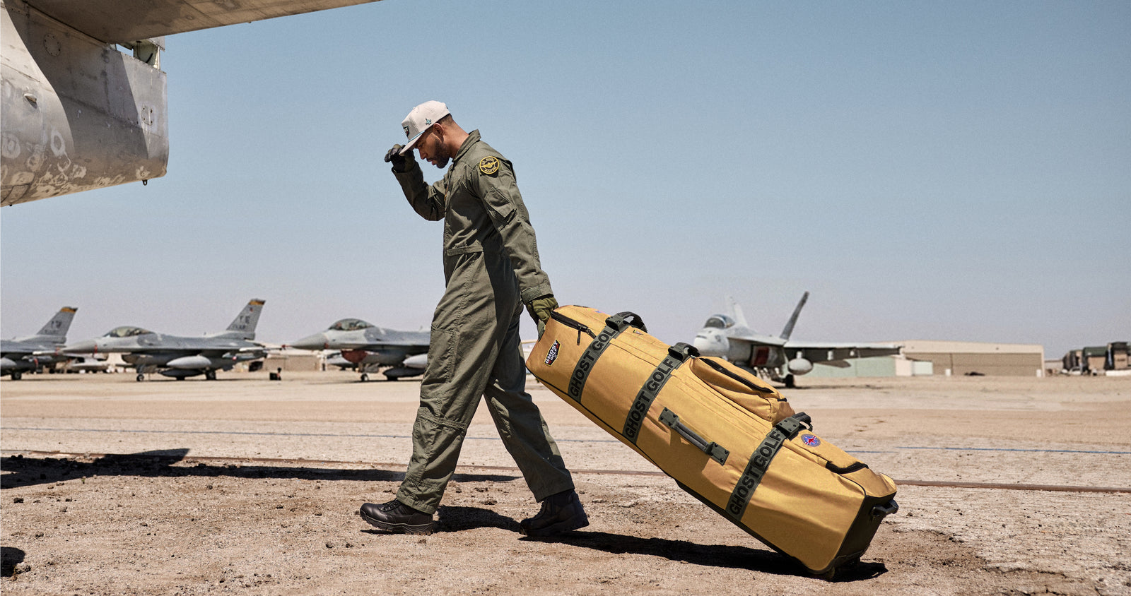 Lifestyle photo of a Black male model walking across an airfield while carrying an AWOL Travel Bag. Fighter jets in the background create an aviation-inspired setting, emphasizing the bag's travel-ready design and premium aesthetic.