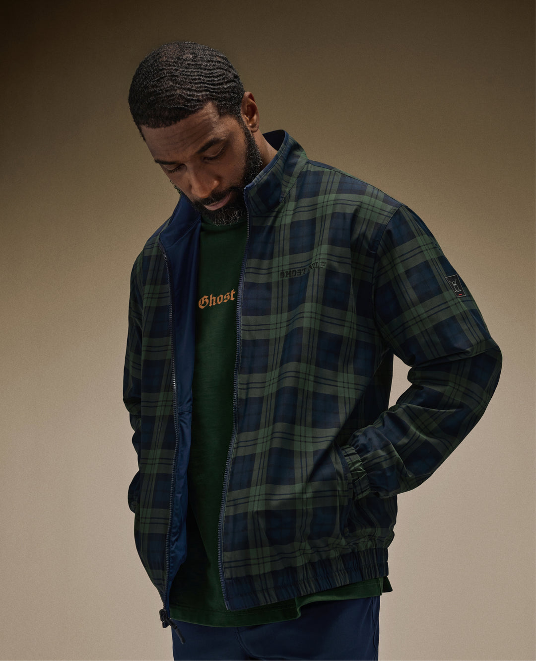 Black Male Model in brown studio setting wearing a reversible jacket with navy pants and green ghost golf tee