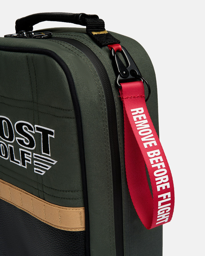 Detail shot of the G-Suit Shoe Bag showcasing a metal carabiner attachment with a signature red "Remove Before Flight" tag. Close-up image highlighting the premium hardware, functional accessory details, and aviation-inspired Ghost Golf design.