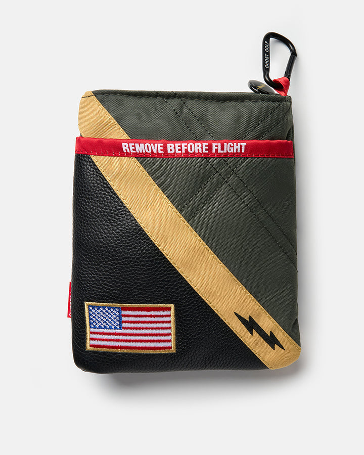 Back product shot of the G-Suit Utility Pouch featuring a USA flag patch in the bottom-left corner and "Remove Before Flight" text centered near the top. Rear-facing view highlighting the pouch’s military-inspired design details and branding elements.