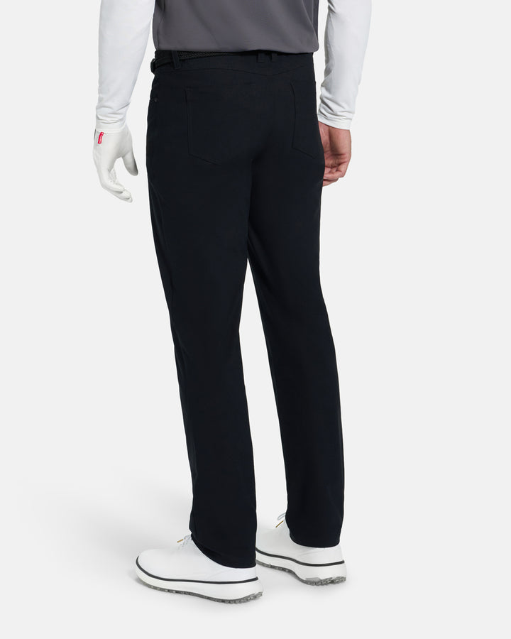 Back View of Black Ghost Golf Core 5 Pocket Pant on White Male Model with white shoes #color_black
