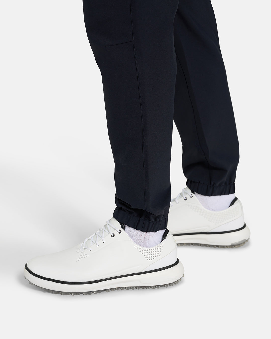 Bottom Closeup Side View of Black Ghost Golf Core Jogger Pant on White Male Model with white shoes #color_black
