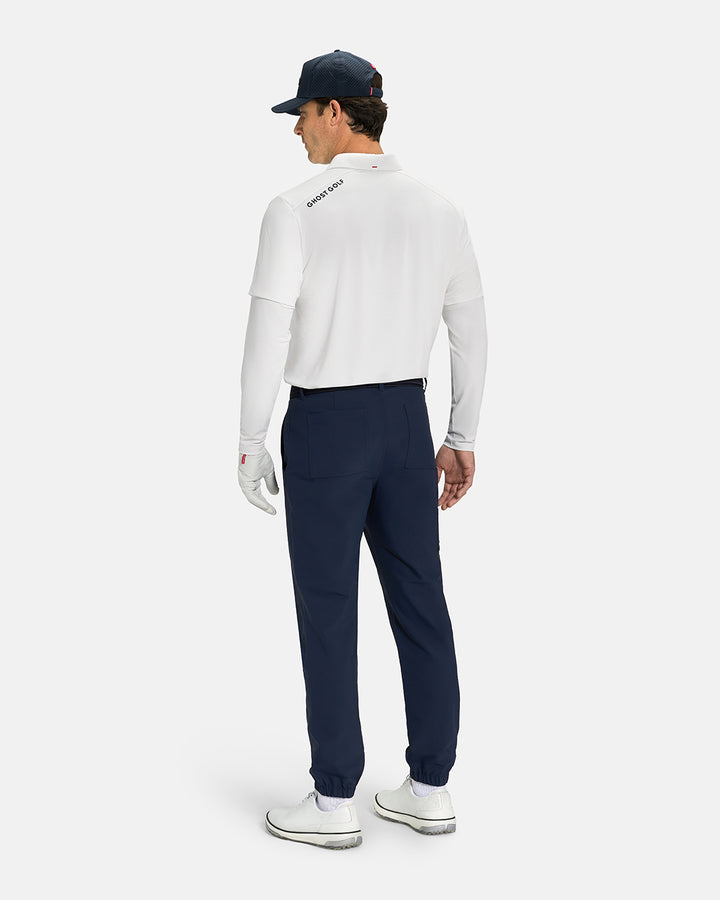 Back Full Body Front View of Navy Ghost Golf Core Jogger Pant on White Male Model wearing white polo navy belt and white shoes and navy hat #color_navy