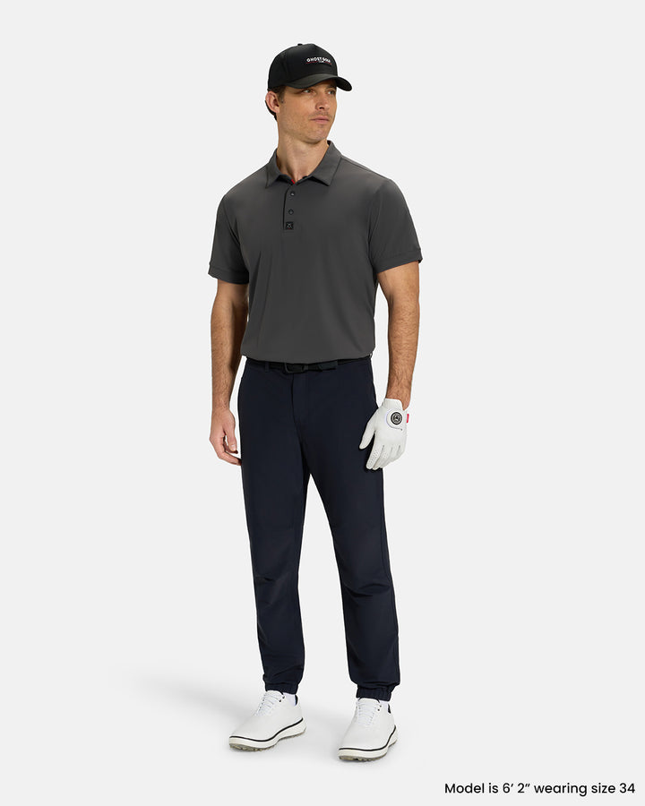 Full Body View of Black Ghost Golf Core Jogger Pant on White Male Model wearing grey polo white gloves black belt white shoes and black hat #color_black