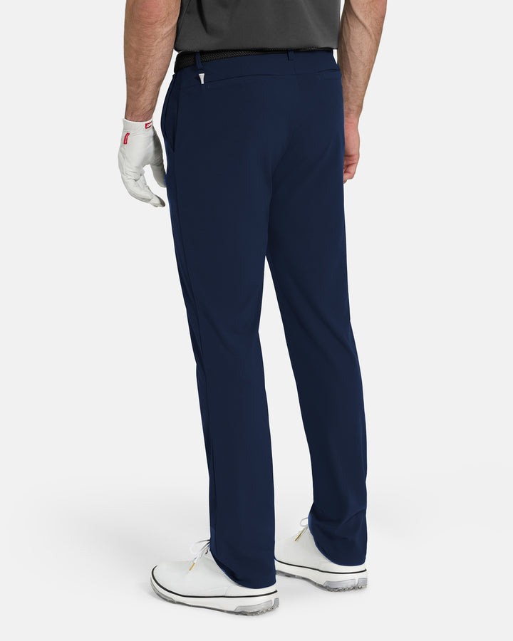 Back View of Navy Ghost Golf Core Pant on White Male Model with white shoes #color_navy