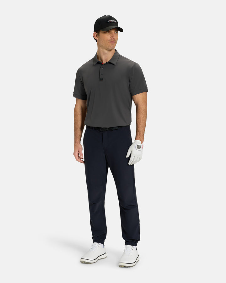 Full Body View of Iron Grey Ghost Golf Core Polo Tucked on White Male Model wearing black pants white gloves black belt white shoes and black hat #color_iron-grey