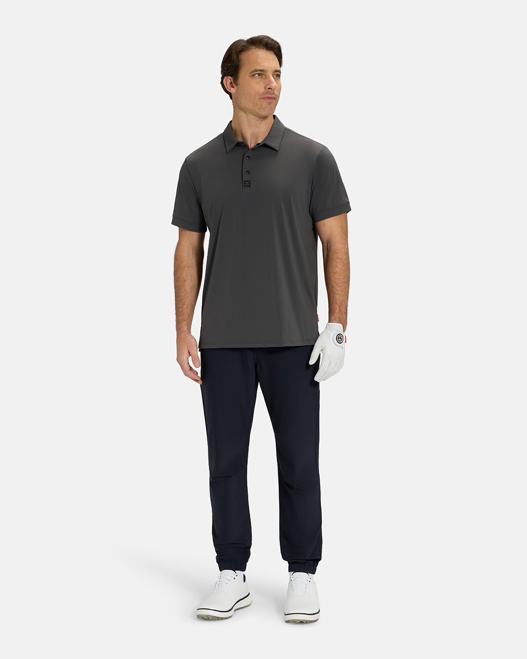 Full Body View of Iron Grey Ghost Golf Core Polo Untucked on White Male Model wearing black pants white gloves and white shoes #color_iron-grey