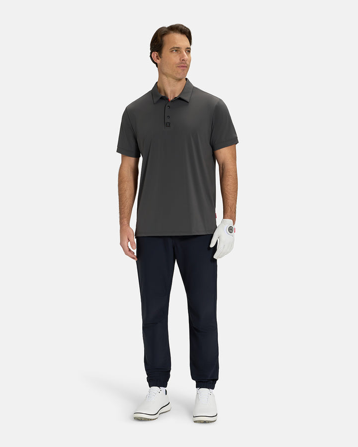 Full Body View of Iron Grey Ghost Golf Core Polo Untucked on White Male Model wearing black pants white gloves and white shoes #color_iron-grey