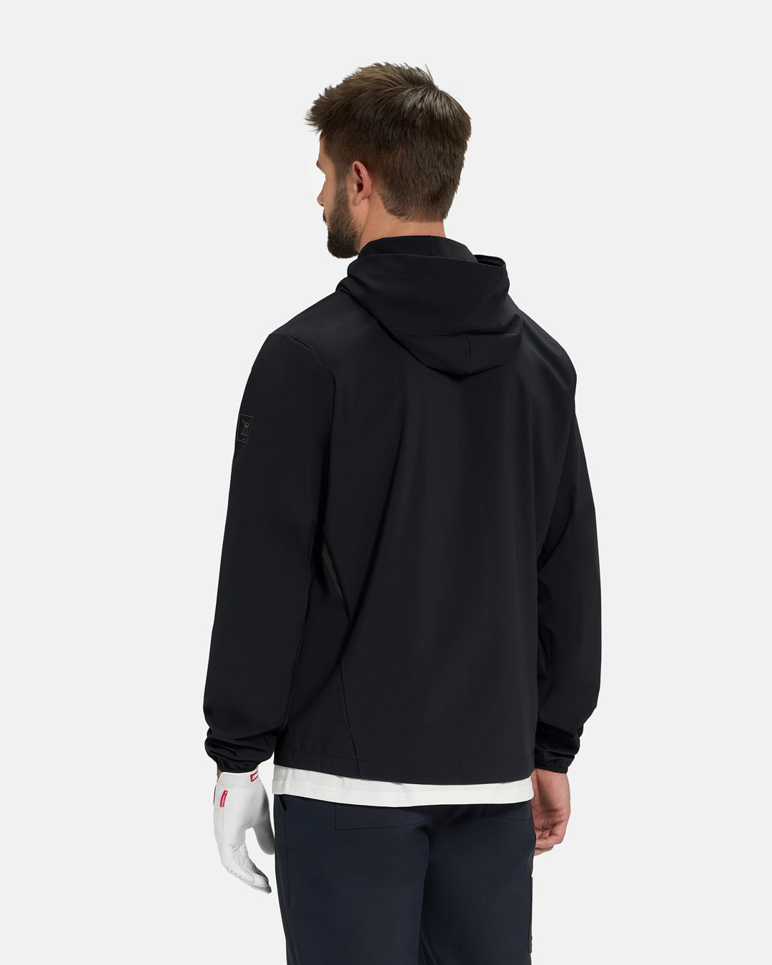 Back View of Black Ghost Golf Hooded Zip Shell Jacket on White Male Model wearing white glove and black pants #color_black