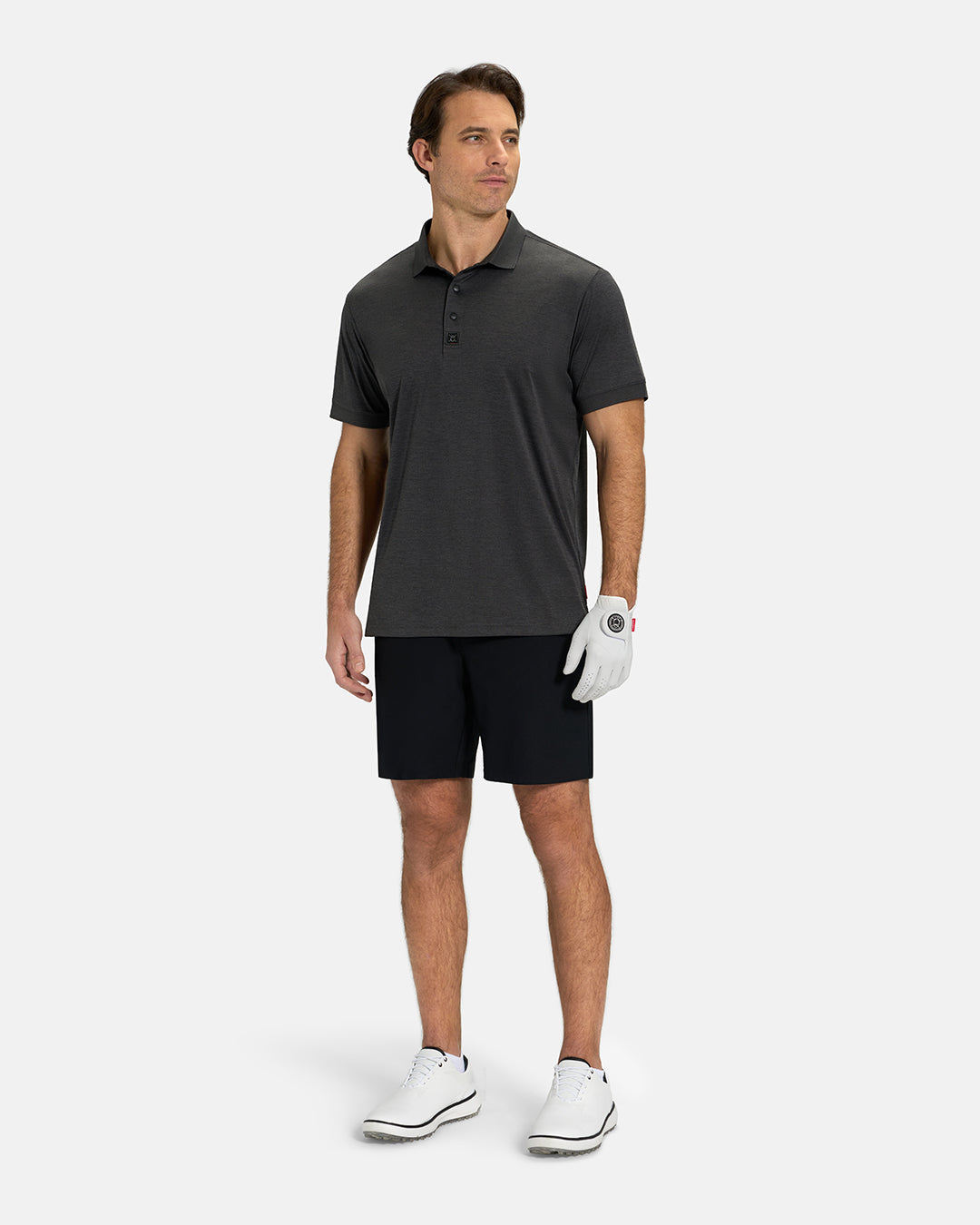 Full Body View of Iron Grey Ghost Golf Marled Core Logo Untucked on White Male Model wearing black shorts white gloves and white shoes #color_iron-grey