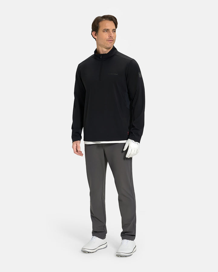 Full Body View of Black Ghost Golf Quarter Zip Mock Jacket on White Male Model wearing grey pants white glove white tee and white shoes #color_black