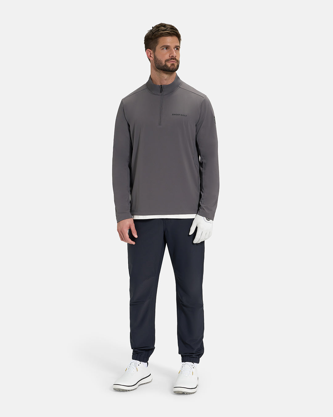 Full Body View of Iron Grey Ghost Golf Quarter Zip Mock Jacket on White Male Model wearing navy pants white glove white tee and white shoes #color_iron-grey