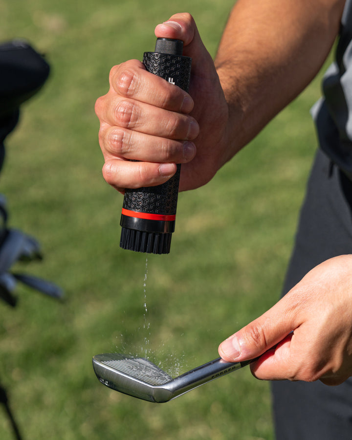 Golfer using the water pump on golf brush to clean golf club #color_black