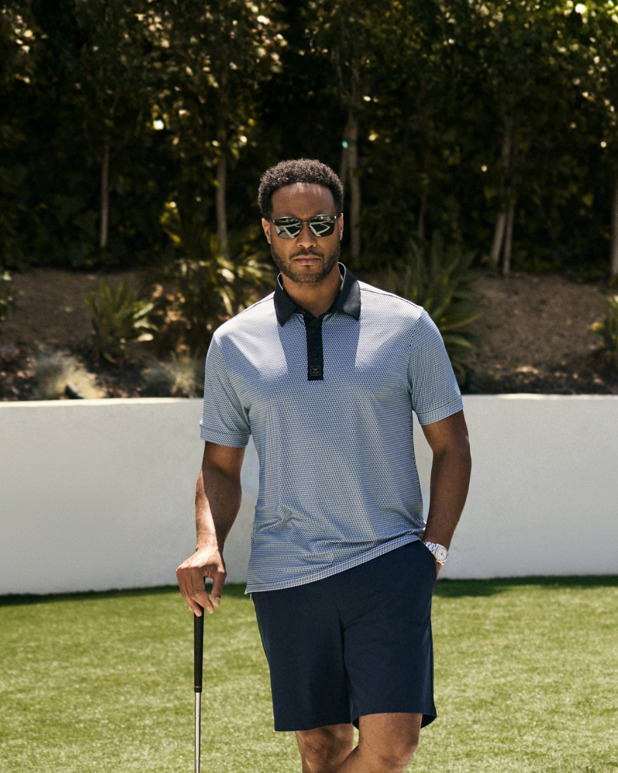 A male model stands poolside holding a golf club with a confident pose