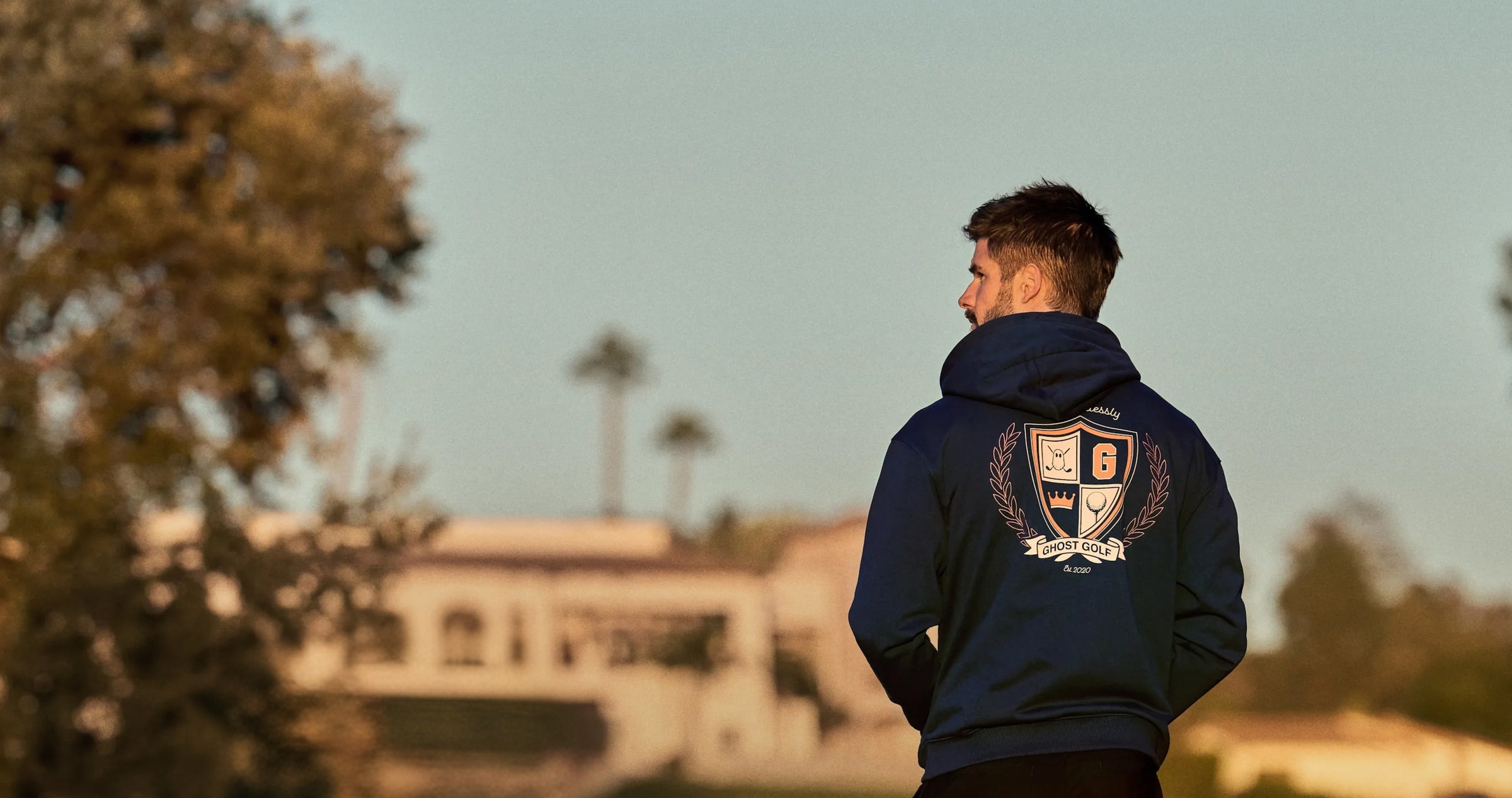 Male Model with back facing a hoodie with a ghost golf graphic on the back looking towards his left