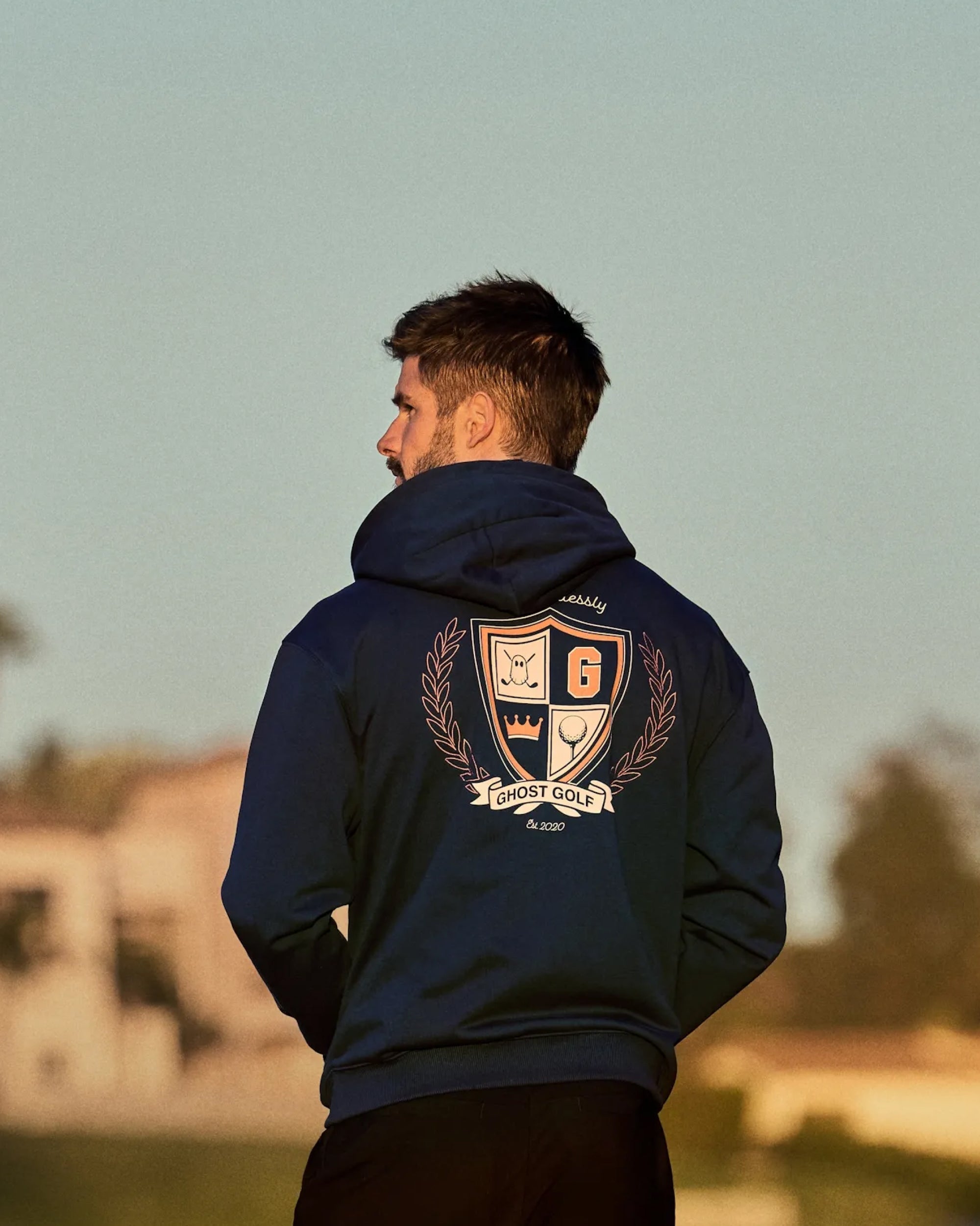 Male Model with back facing a hoodie with a ghost golf graphic on the back looking towards his left