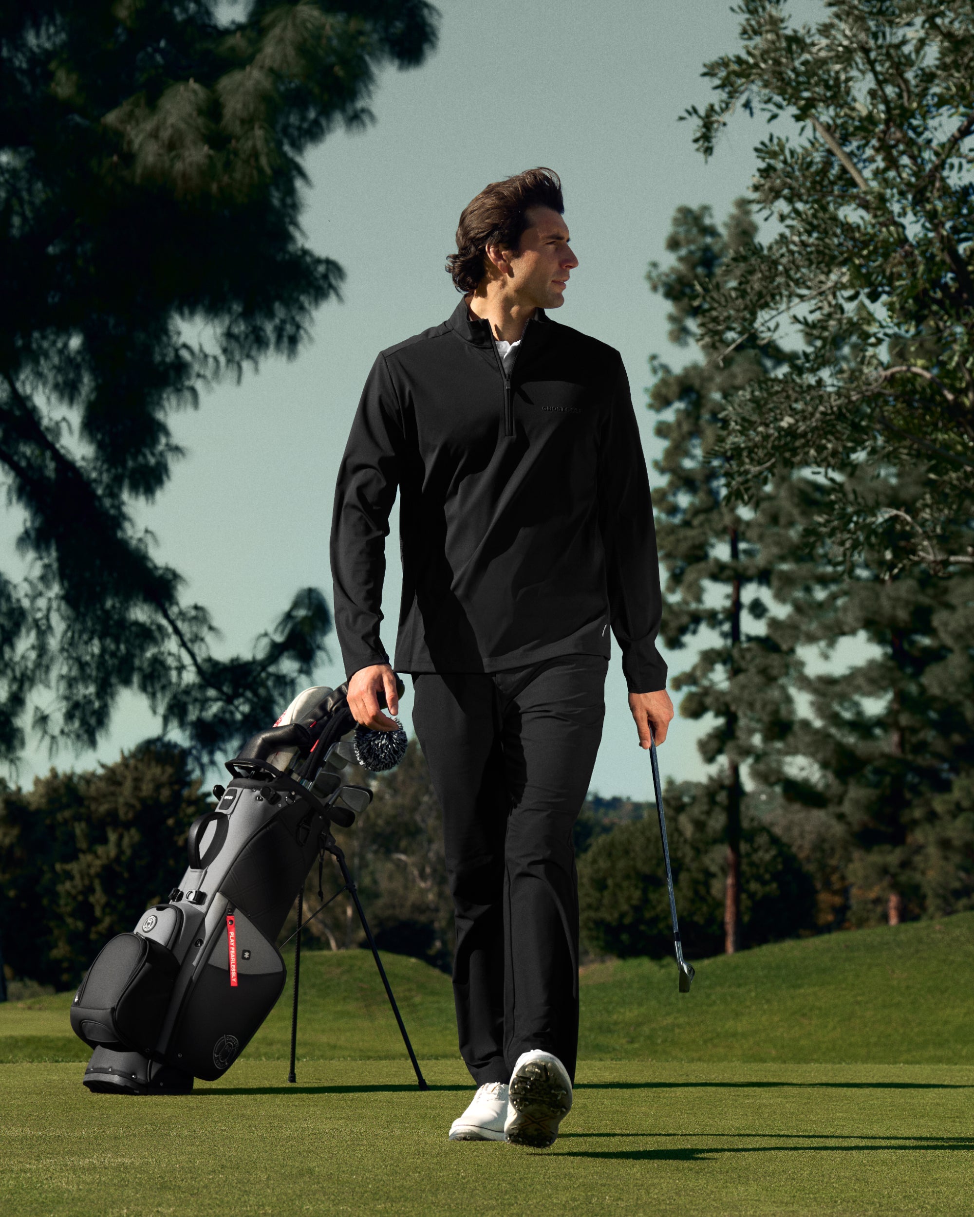 Man walking on a golf course with a golf club and golf bag in the background