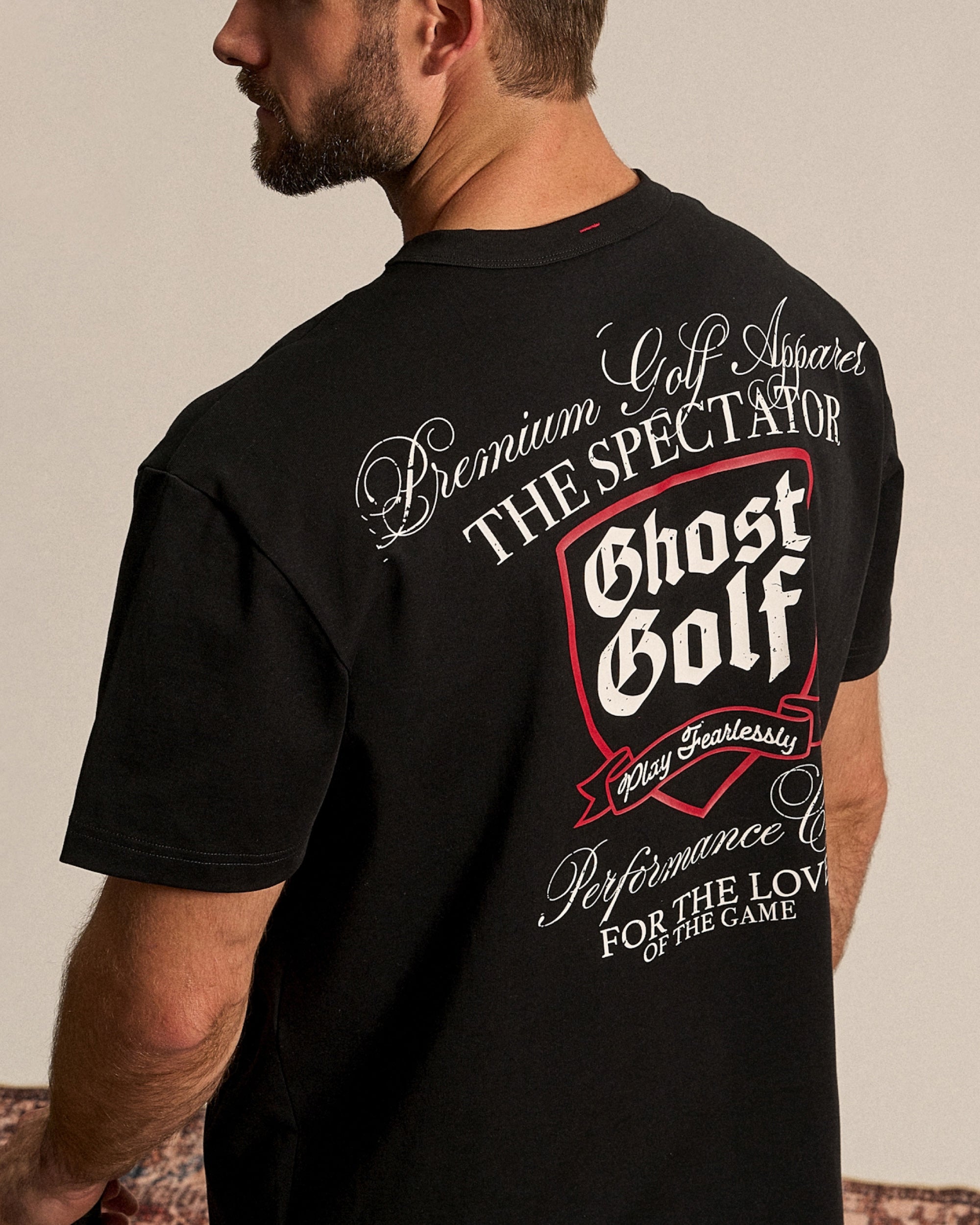 White Male in studio, back facing, wearing a black Ghost Golf graphic tee.