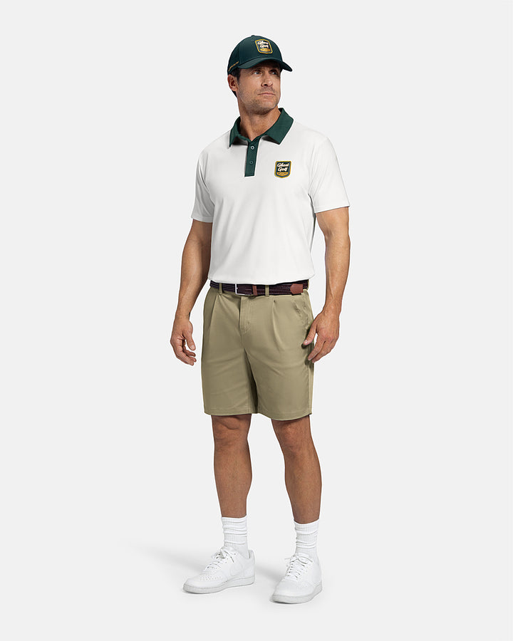 Man wearing a beige polo shirt, khaki shorts, white sneakers, and a green cap on a white background #color_cream-white