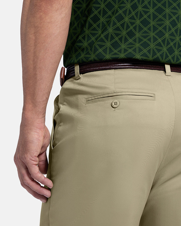 Closeup Back View of Sand Patrons Pleated Pant on white male model with green polo tucked in wearing brown belt #color_sand
