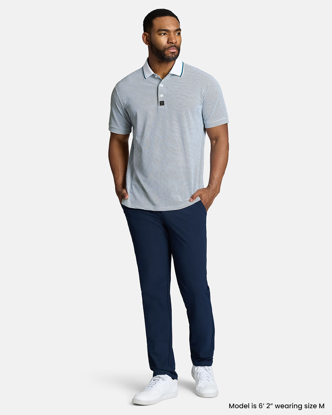 Full Body Front Shot of Black Male Model Wearing White Qualifier Flag Polo with navy pants and white shoes. Polo is untucked. #color_white