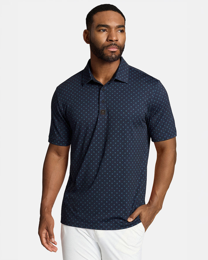 Top Front Body Shot of Black Male Model Wearing Navy Qualifier Geo Polo with white pants. Polo is untucked #color_navy