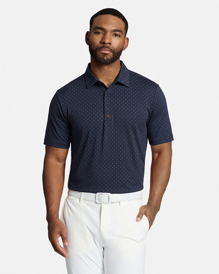 Top Front Body Shot of Black Male Model Wearing Navy Qualifier Geo Polo with white pants and white belt. Polo is tucked #color_navy