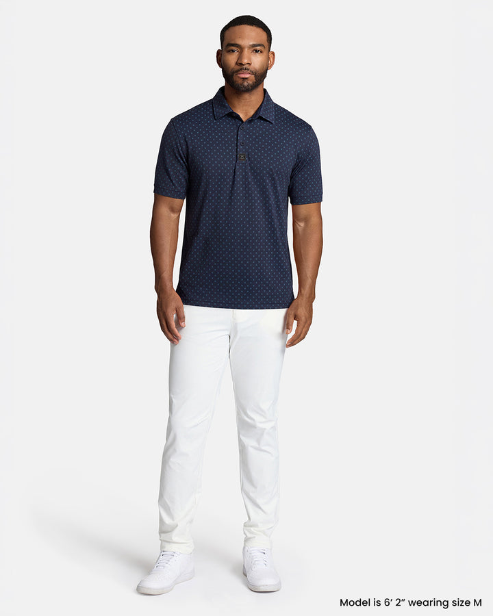 Full Front Body Shot of Black Male Model Wearing Navy Qualifier Geo Polo with white pants and white shoes #color_navy
