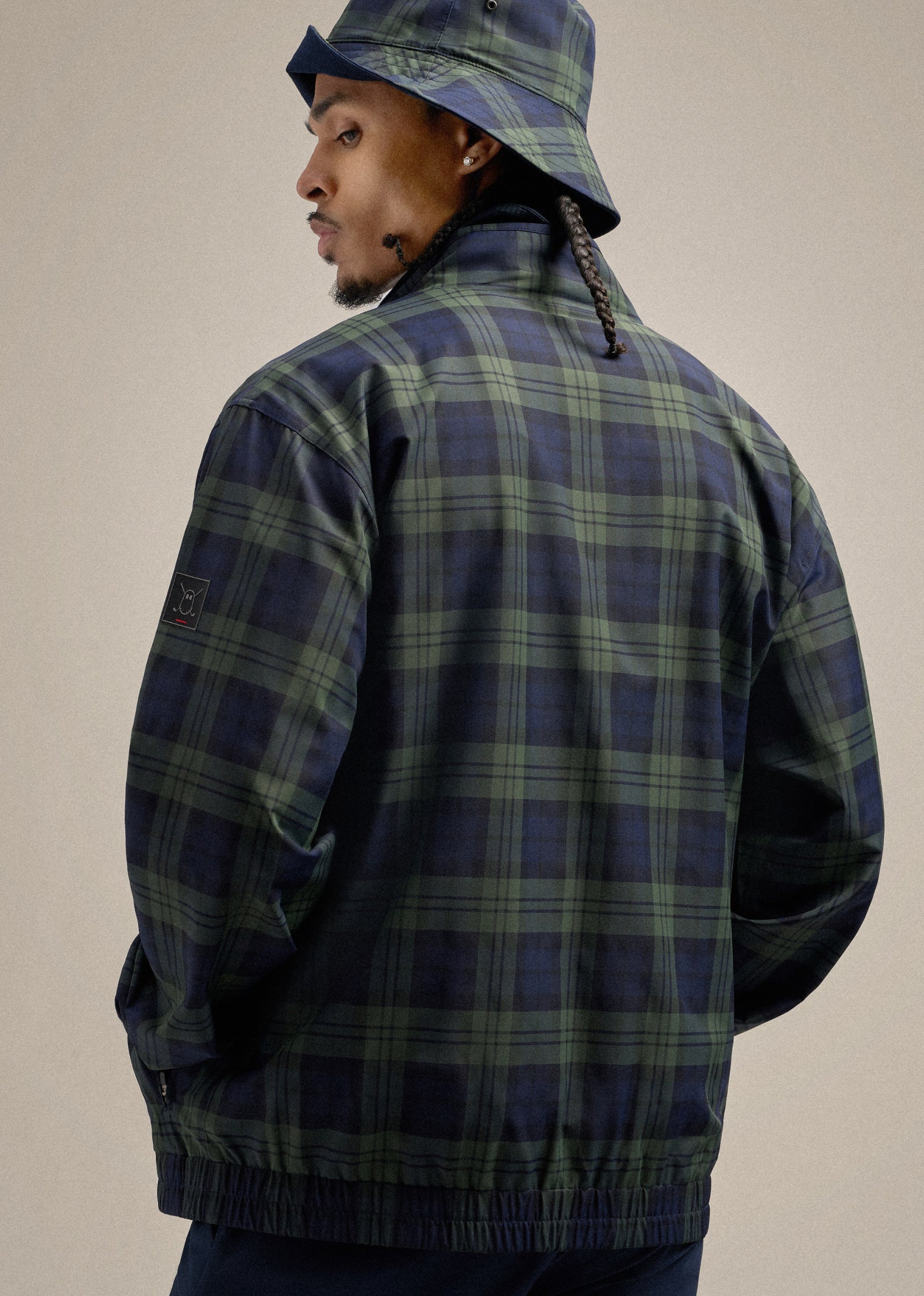 Black Male model wearing a plaid bucket hat and matching jacket, shown from the back while looking over his left shoulder, creating a stylish and dynamic pose.