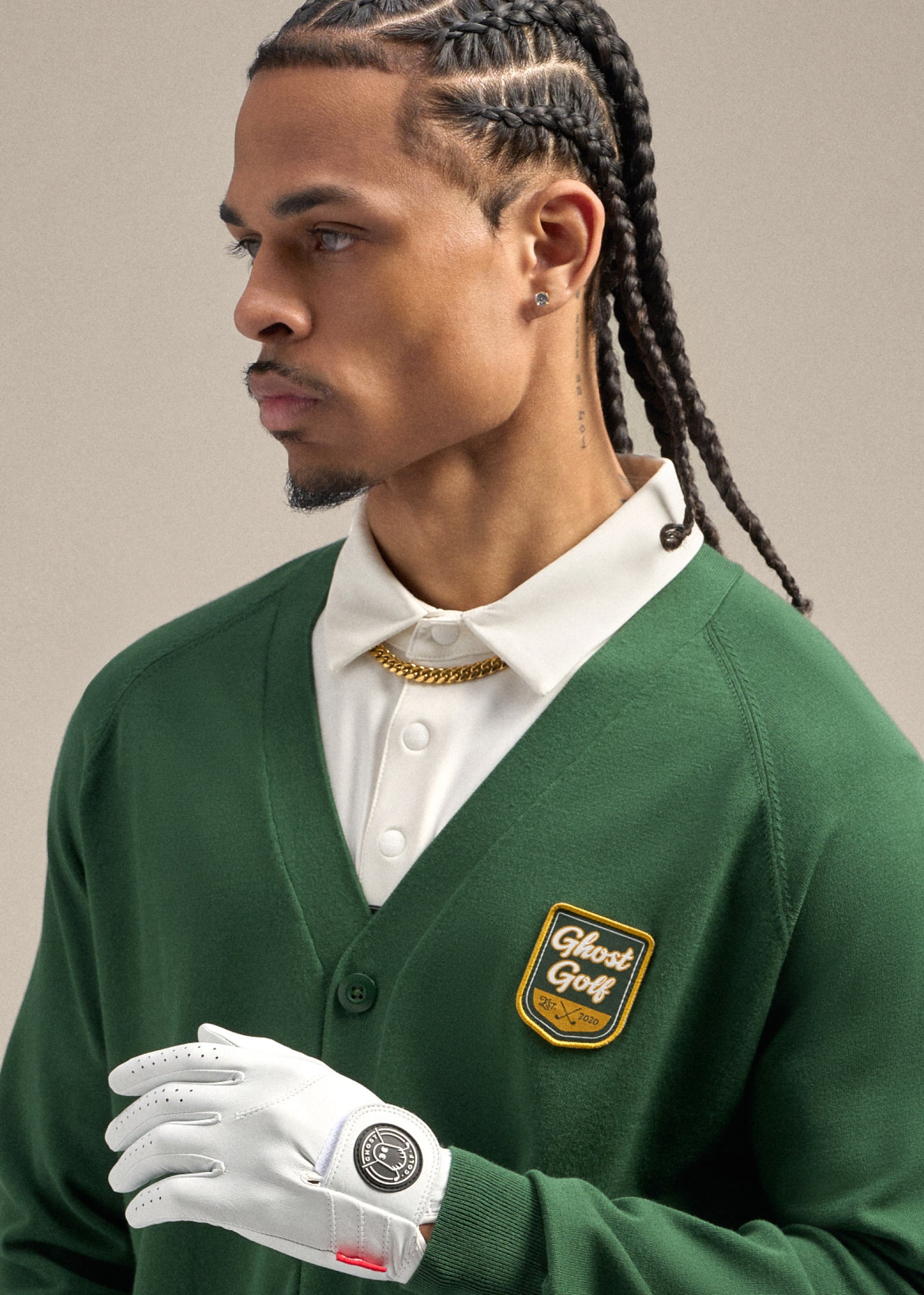 Close-up of a Black male model wearing a green cardigan over a white polo shirt. He is wearing a gold chain, with a white golf glove held in front of him, creating a clean and stylish golf-inspired look.