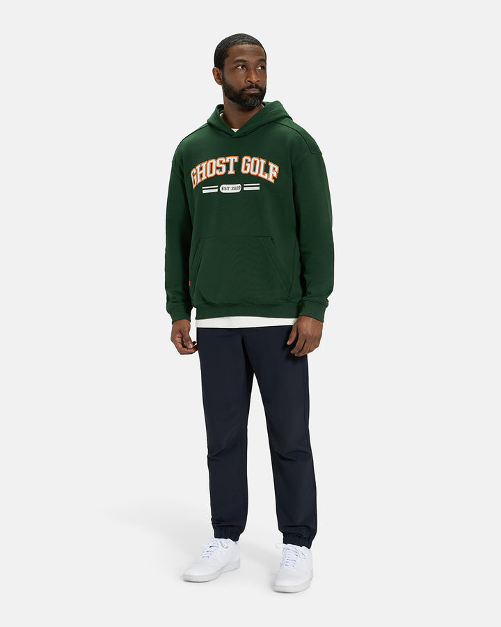 Full Body View of Bogey Green Spectator Dormie Hoodie on Black Male Model wearing white tee black pants and white shoes #color_bogey-green