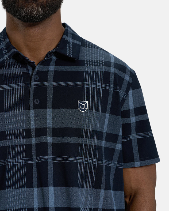 Closeup Front View of Navy Spectator Plaid Polo on Black Male Model with Ghost Icon Crest on chest. #color_navy
