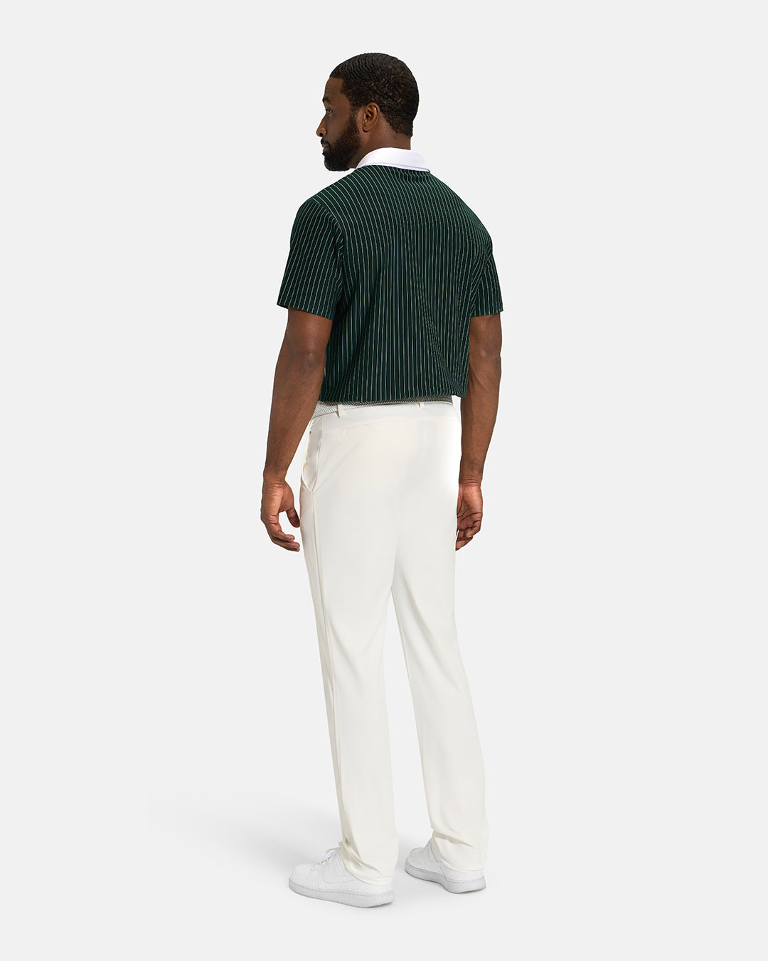 Full Body Back View of Bogey Green Spectator Stripe Polo Tucked on Black Male Model wearing white pants white belt and white shoes #color_bogey-green