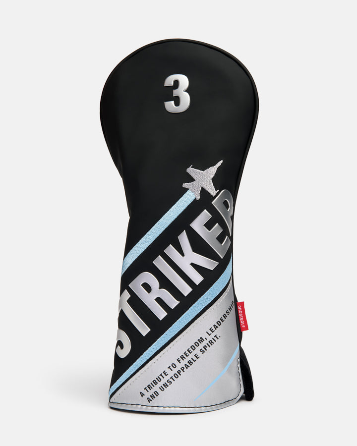 Front product shot of the Striker Tertiary 3 Wood Head Cover featuring oversized Striker typography across the front, with a fighter jet graphic wrapping around the cover. The design also includes a small tribute text detail, showcasing aviation-inspired artwork, premium embroidery. #size_3-wood