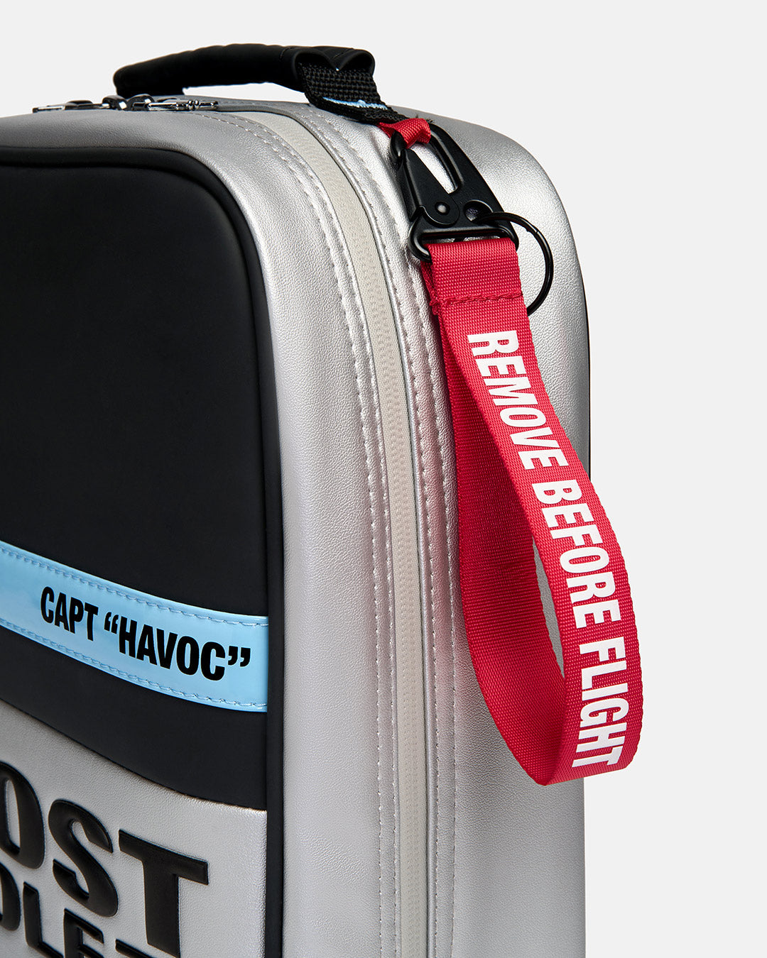 Detail shot of the Striker Shoe Bag showcasing a metal carabiner attachment with a signature red "Remove Before Flight" tag. Close-up image highlighting the premium hardware, functional accessory details, and aviation-inspired Ghost Golf design.