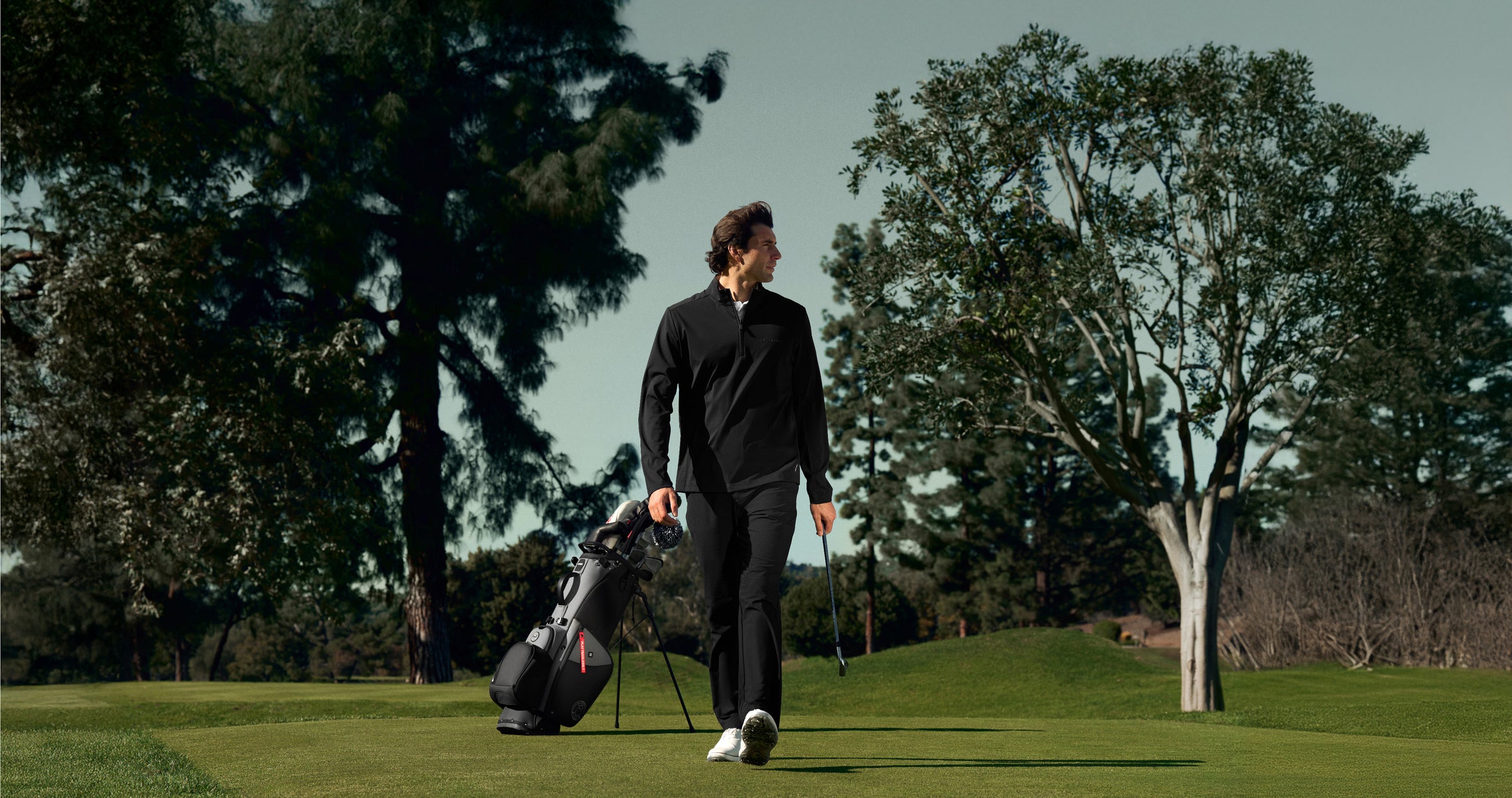 Man walking on a golf course with a golf club and golf bag in the background