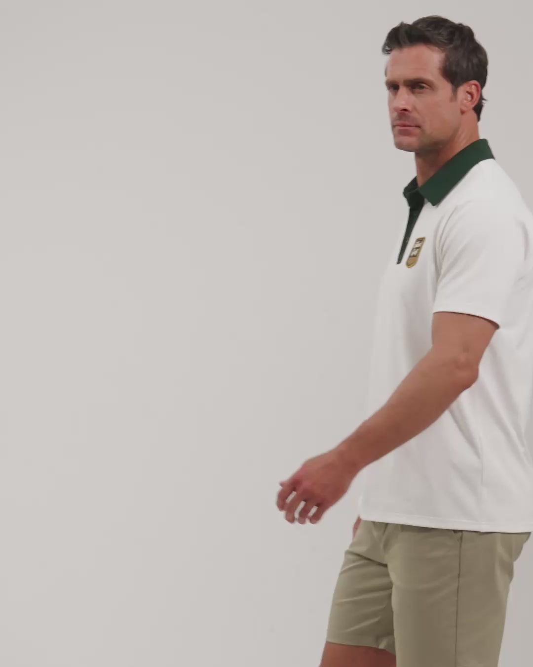 Male model walking naturally showcasing White Patrons Signature Polo from all angles wearing beige shorts and white shoes #color_white