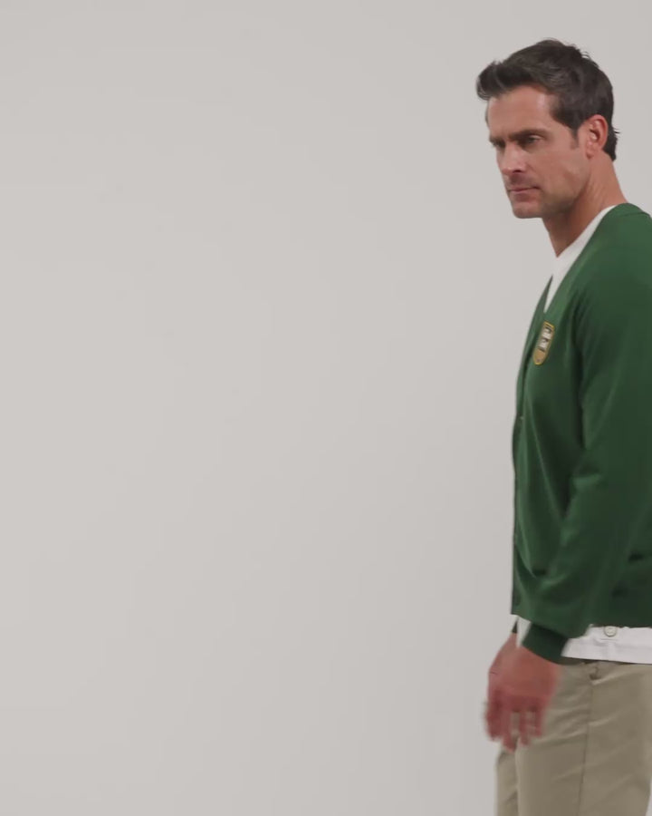 Male model walking naturally showcasing Bogey Green Patrons Sweater Cardigan from all angles wearing beige pants and white tee and shoes #color_bogey-green